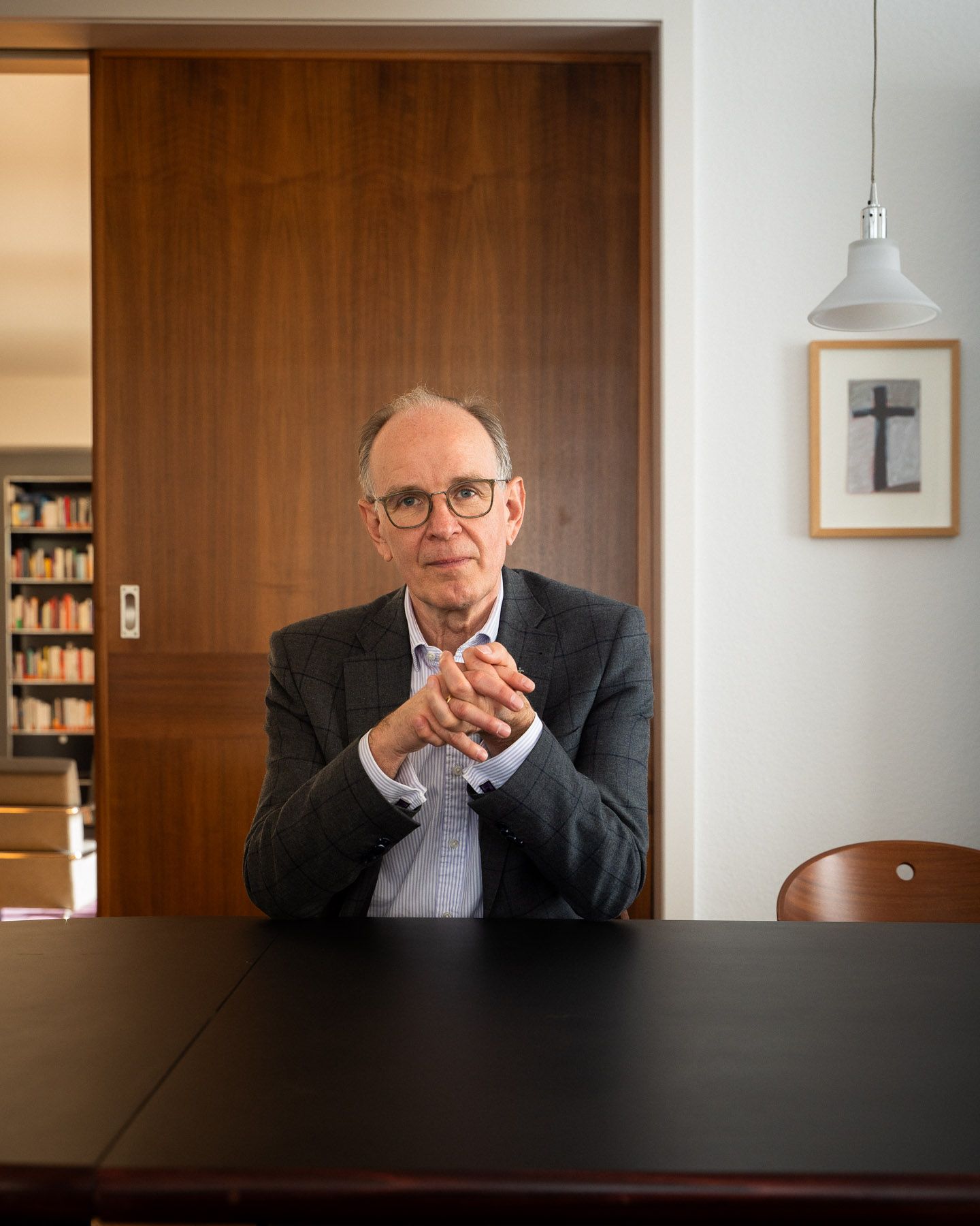Portrait von Landesbischof Ralf Meister an einem Tisch Sitzend in seinem Büro in Hannover. Mit gerahmtem Bild eines Kreuzes im Hintergrund.