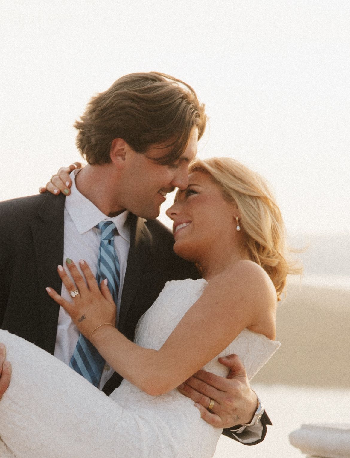 Groom lifts smiling bride in white dress as they share a tender moment at golden hour.
