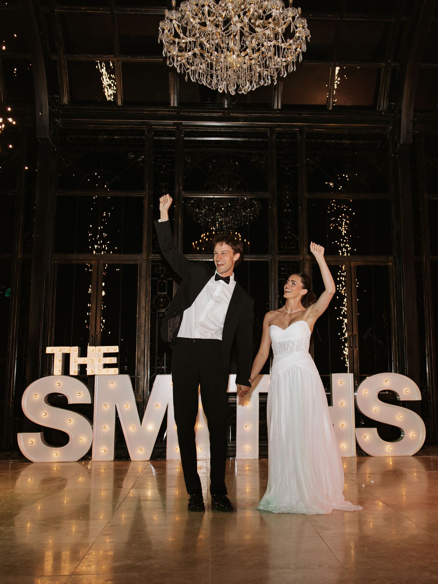 Newlyweds celebrating on dance floor in front of large illuminated THE SMITHS sign.