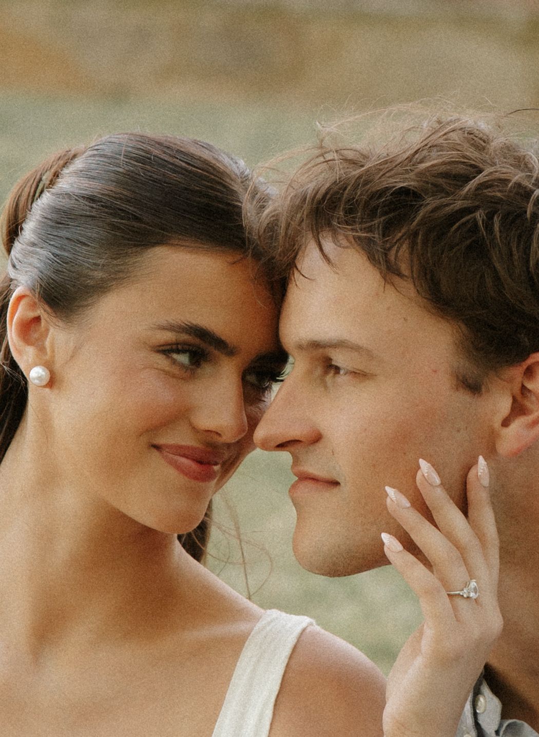 Close-up of an engaged couple nearly kissing, bride wearing pearl earrings and a diamond engagement ring.