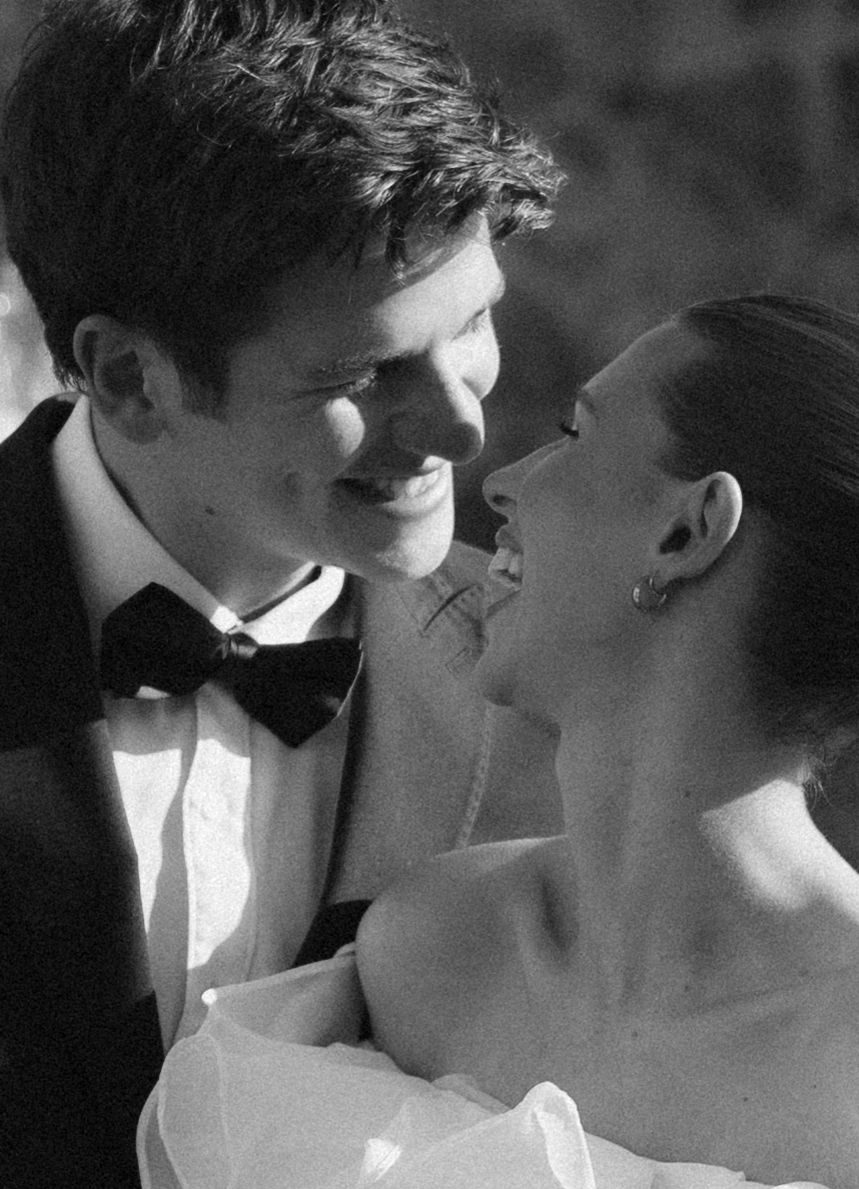 Black and white close-up of smiling groom in bow tie gazing lovingly at bride in strapless wedding gown.