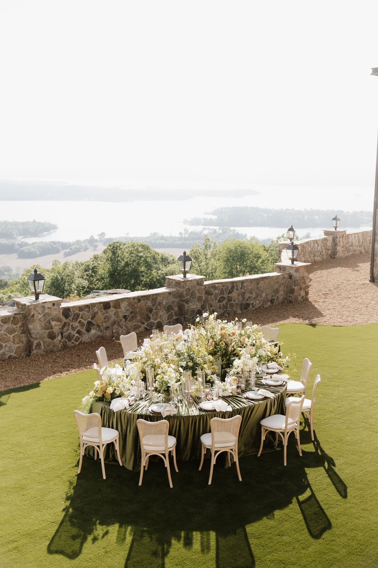 Elegant outdoor wedding reception table with lush white floral centerpiece and green tablecloth overlooking a lake.