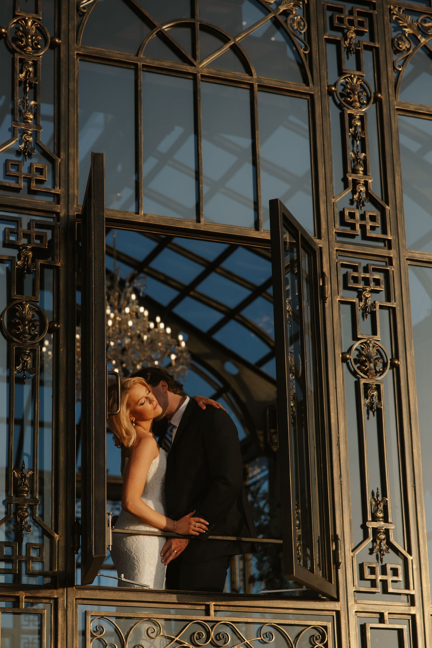 Bride and groom sharing a romantic moment in an ornate gold Art Deco greenhouse doorway.
