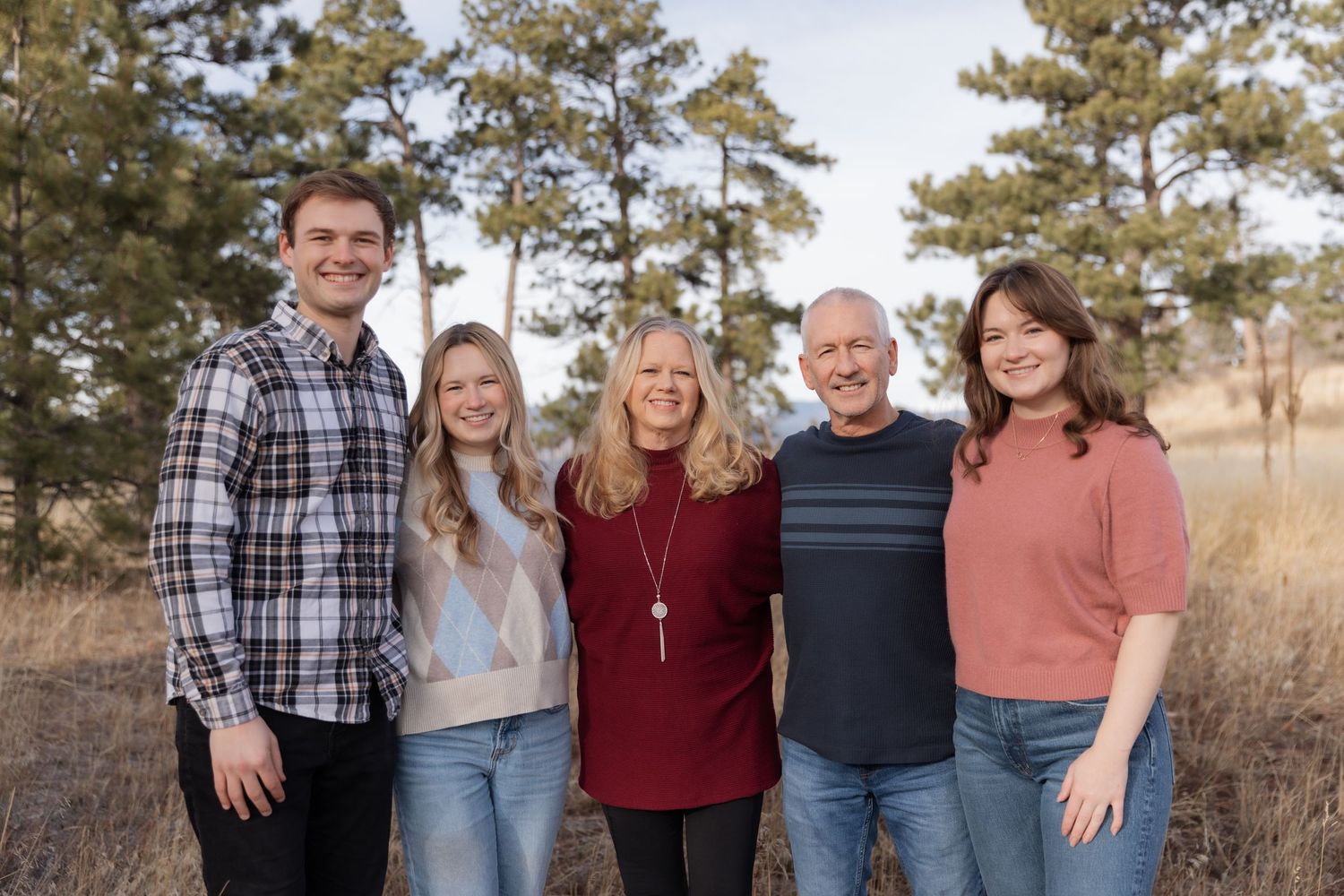 Family of five smiling together in a field with pine trees in Colorado.