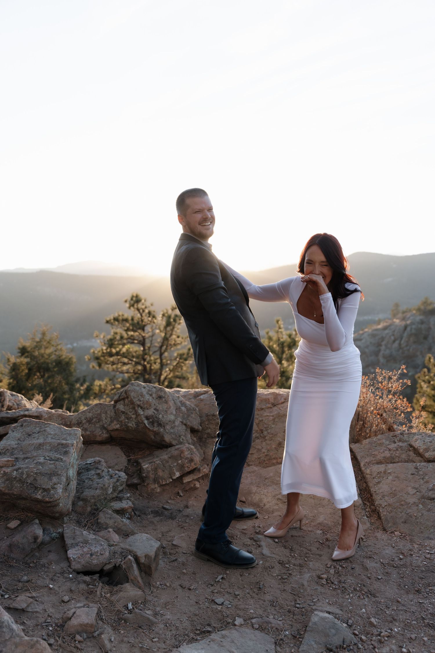 Groom kissing bride's hand at sunset on a rocky Colorado mountain overlook at dusk.