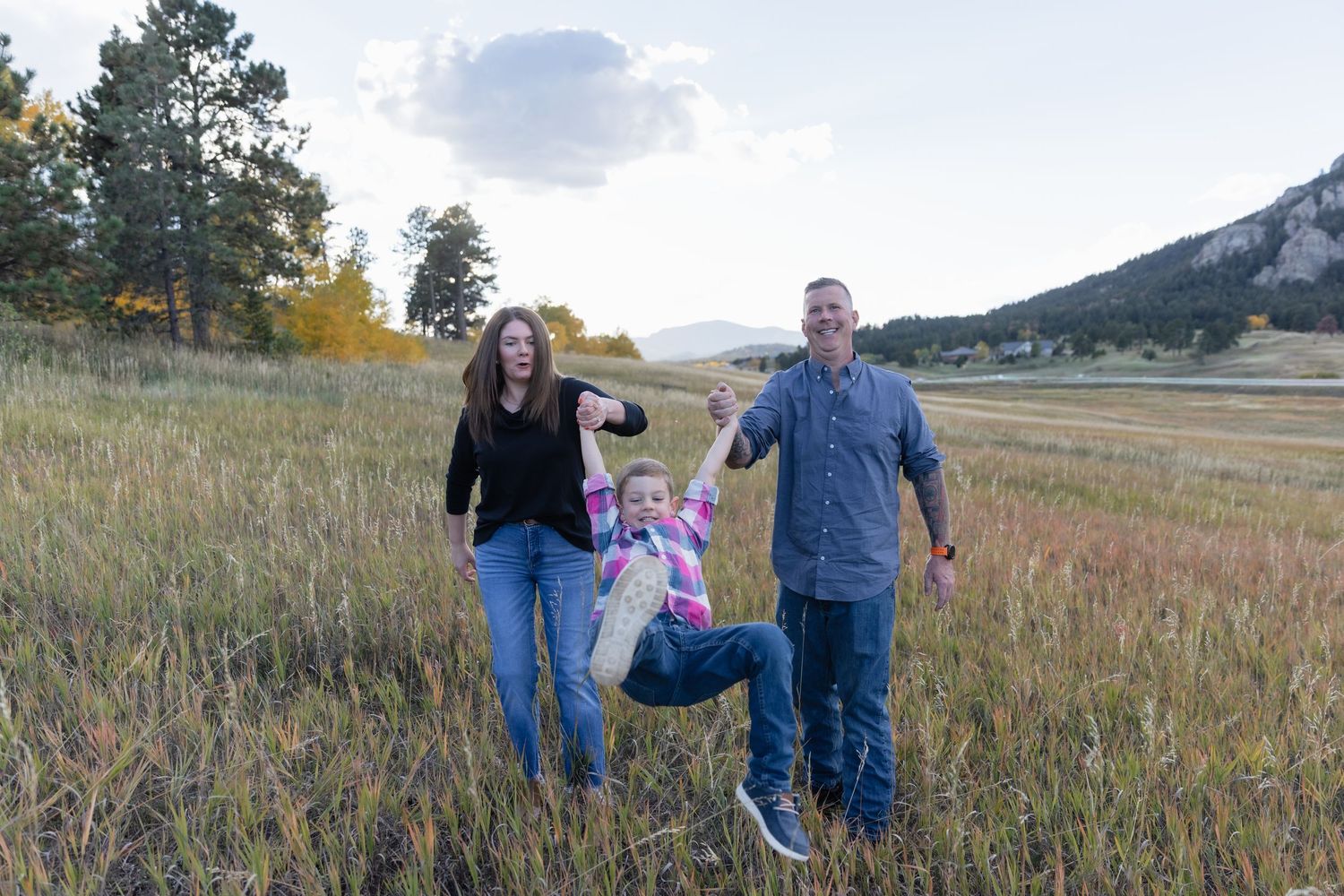 Happy family swinging their child in a golden meadow with mountain views in Colorado.