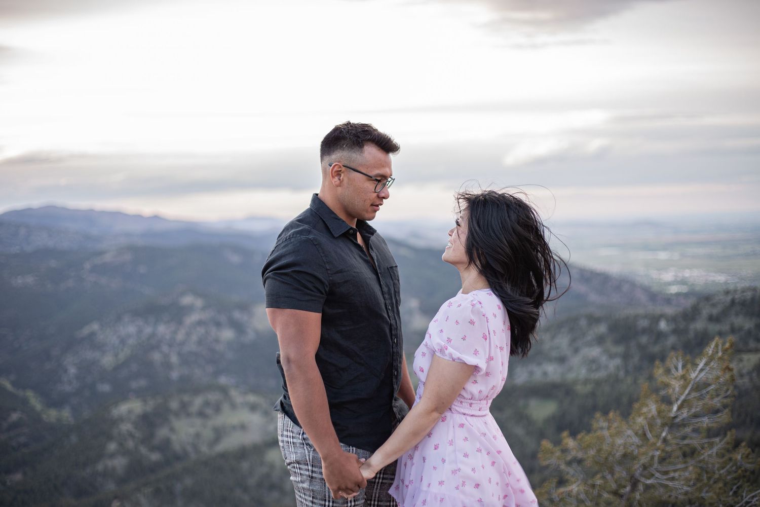 Couple holding hands and gazing at each other on a mountain overlook at sunset.