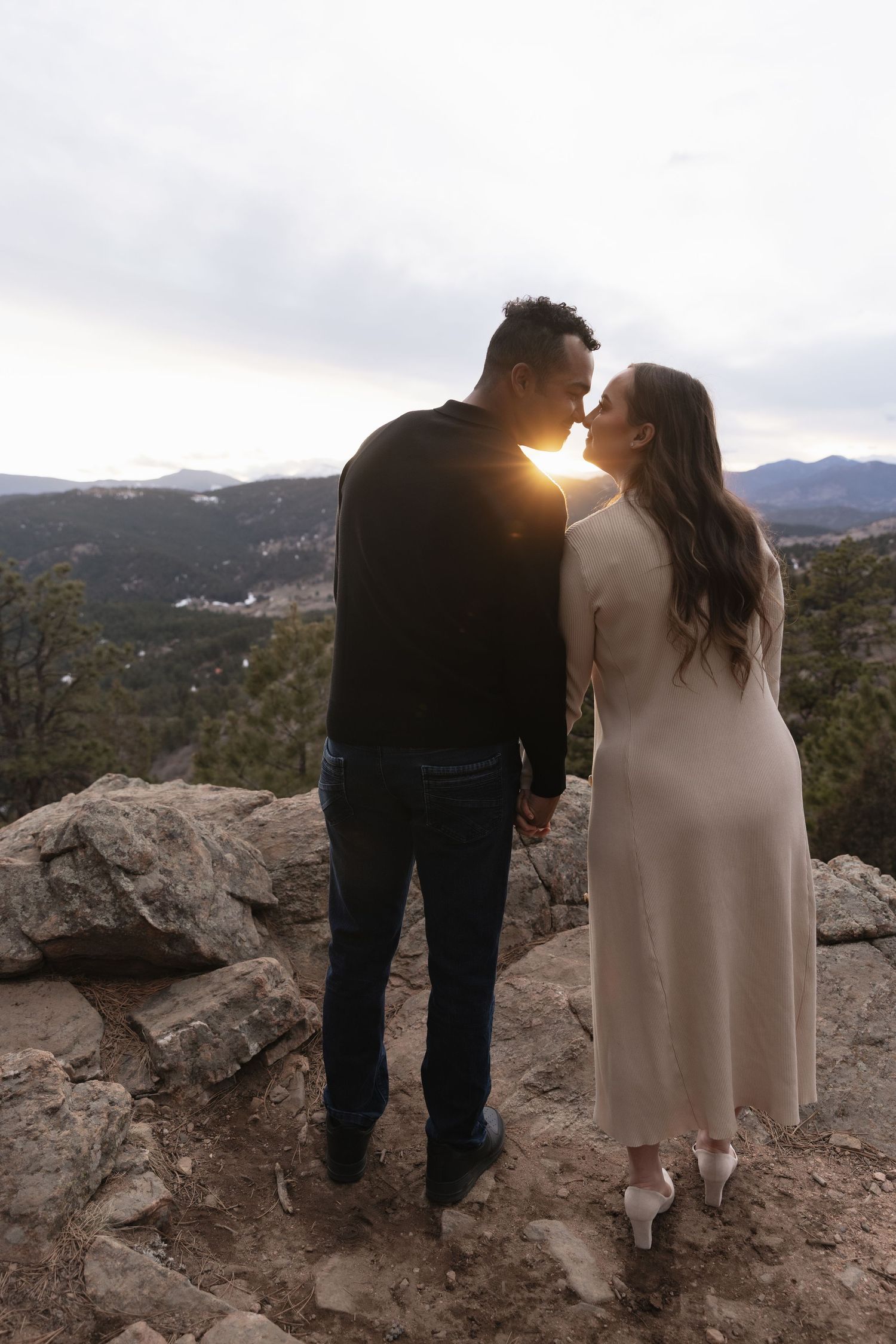 Couple sharing a kiss at sunset on rocky overlook with mountain views in Colorado.