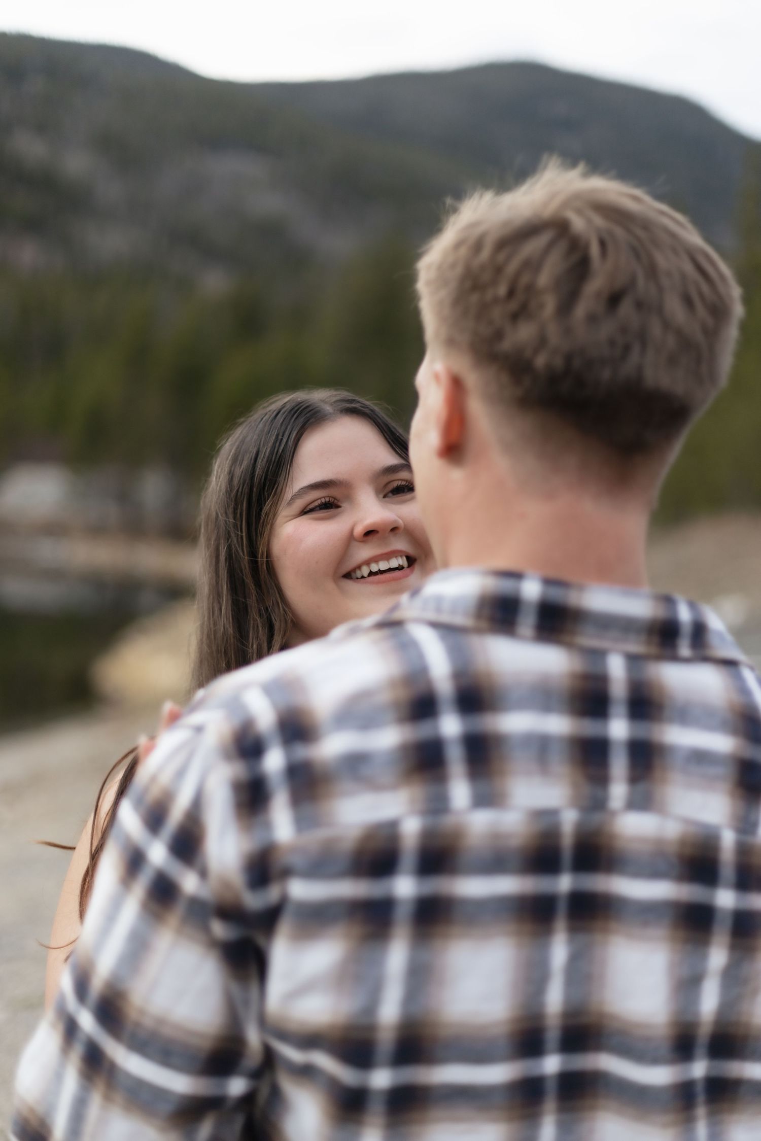Joyful woman laughing while facing her partner during an outdoor mountain engagement photo session.