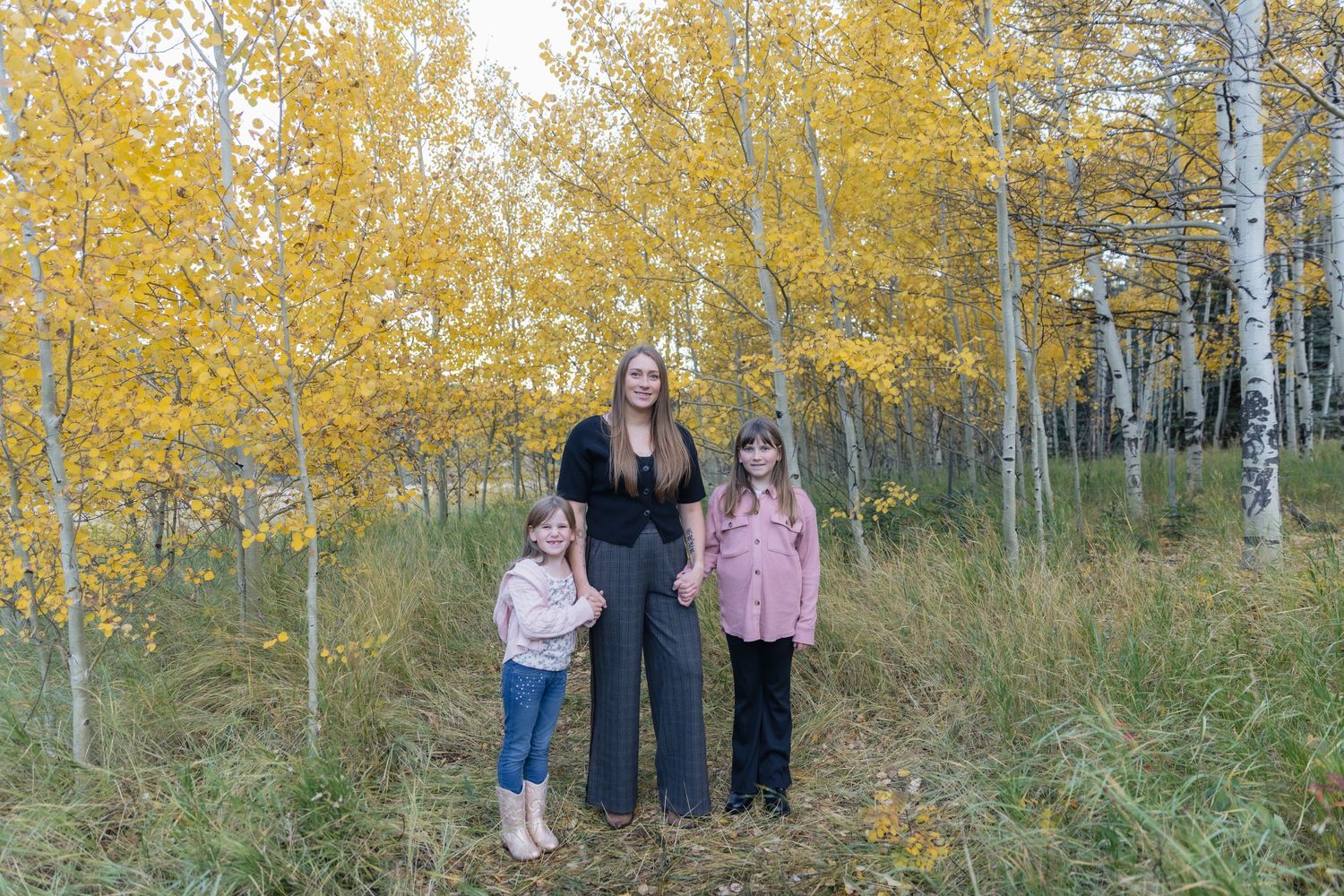 Woman and two girls pose among golden aspen trees in autumn forest.