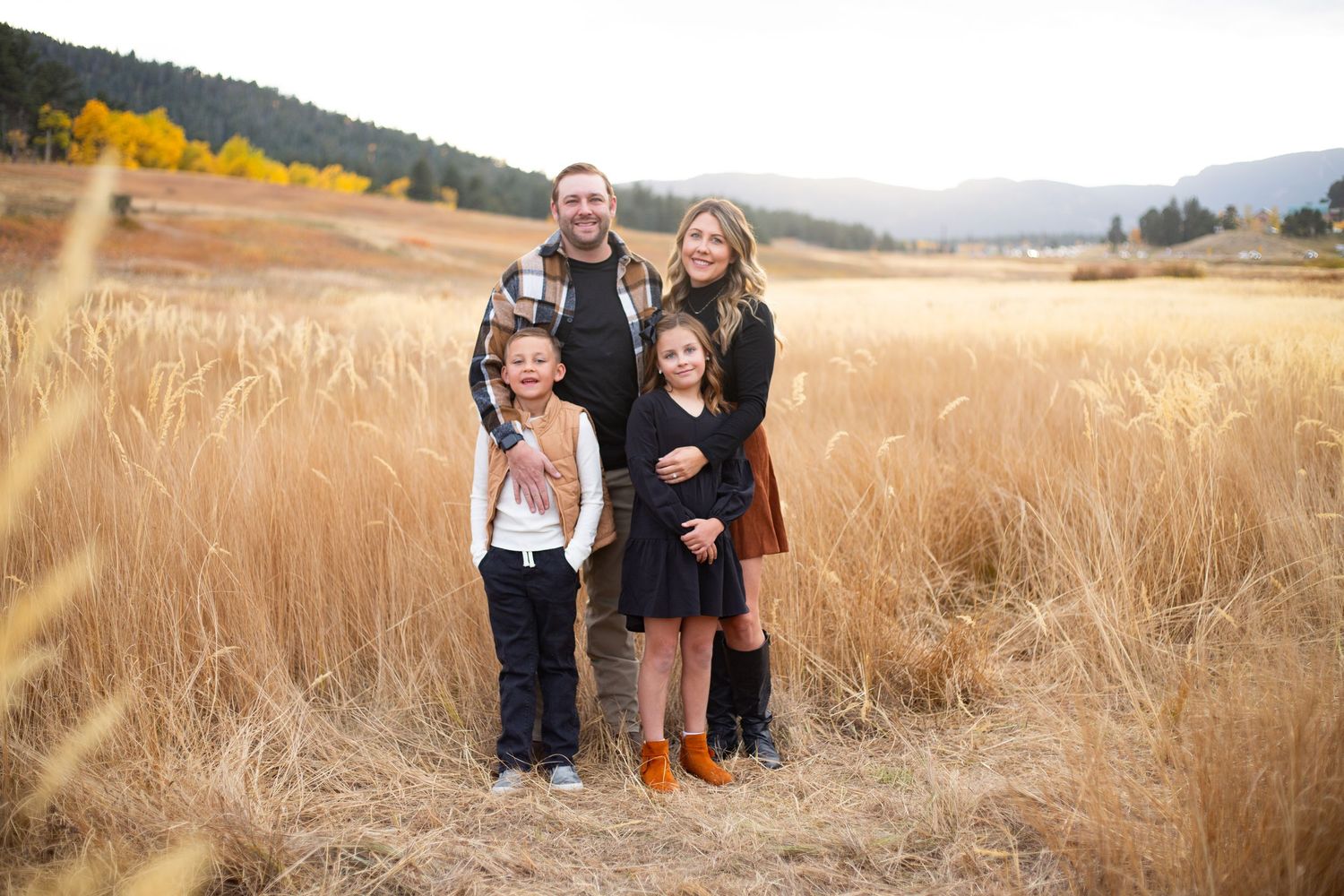 Family of four smiles together in golden autumn meadow field.