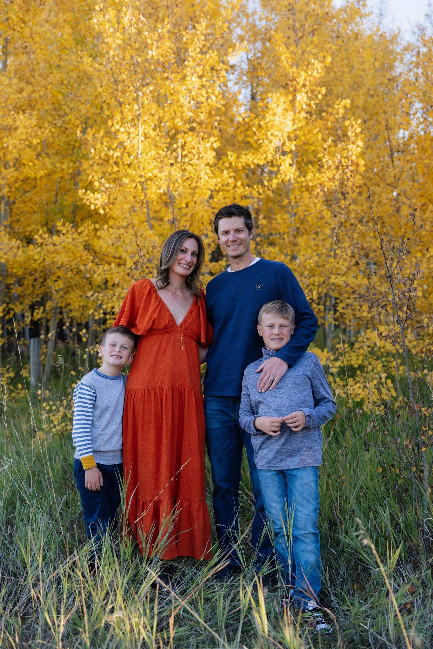 Family of four posing in front of vibrant golden aspen trees in autumn, mother in red dress.