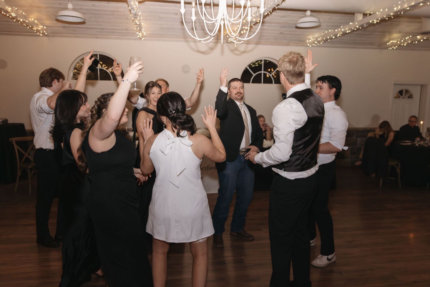Wedding guests celebrate on the dance floor under twinkling lights in a festive reception hall.