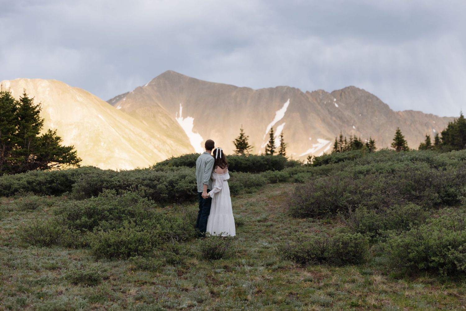 Bride and groom standing together in lush mountain landscape at golden hour sunset.