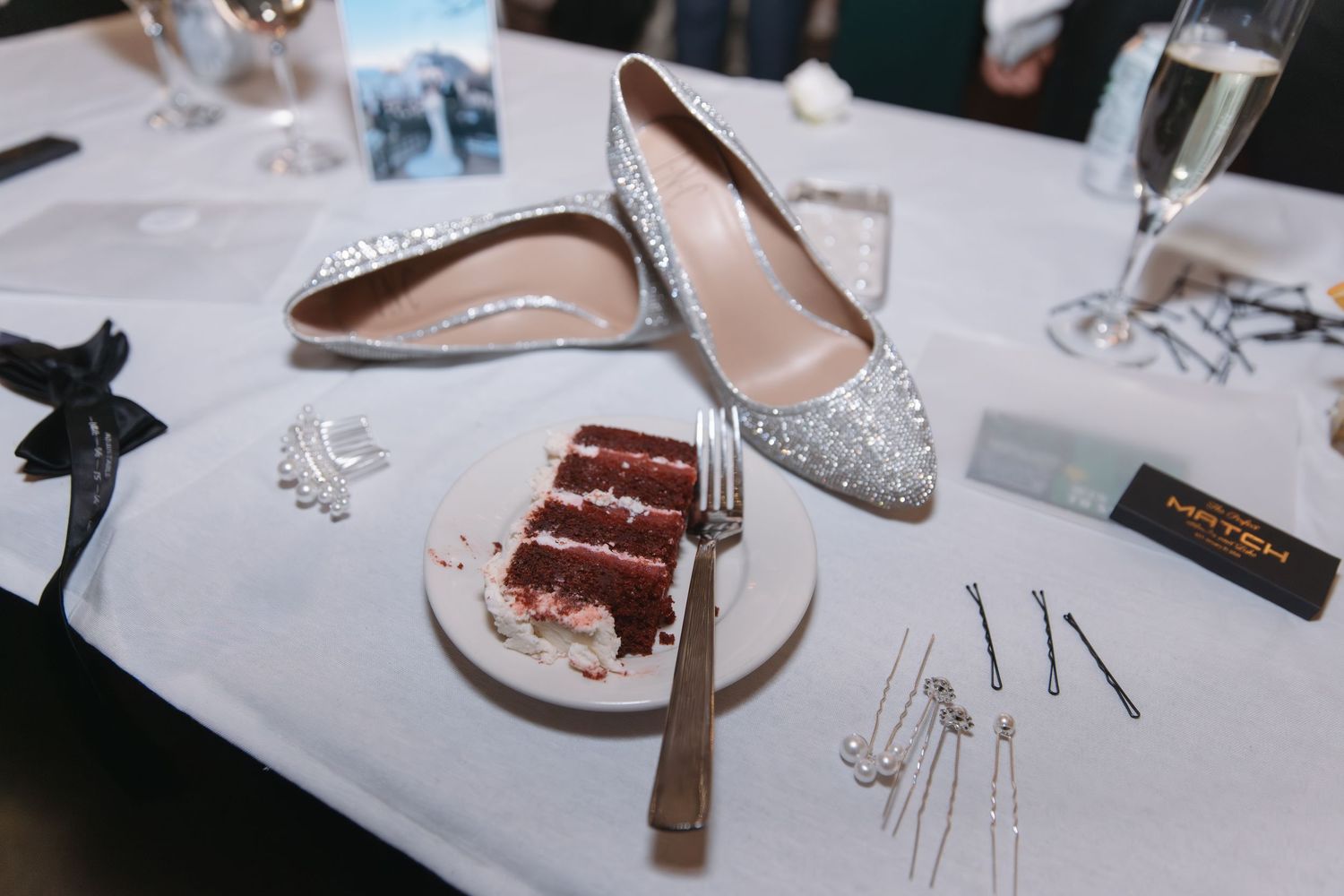 Silver glitter heels beside red velvet cake slice on white table.