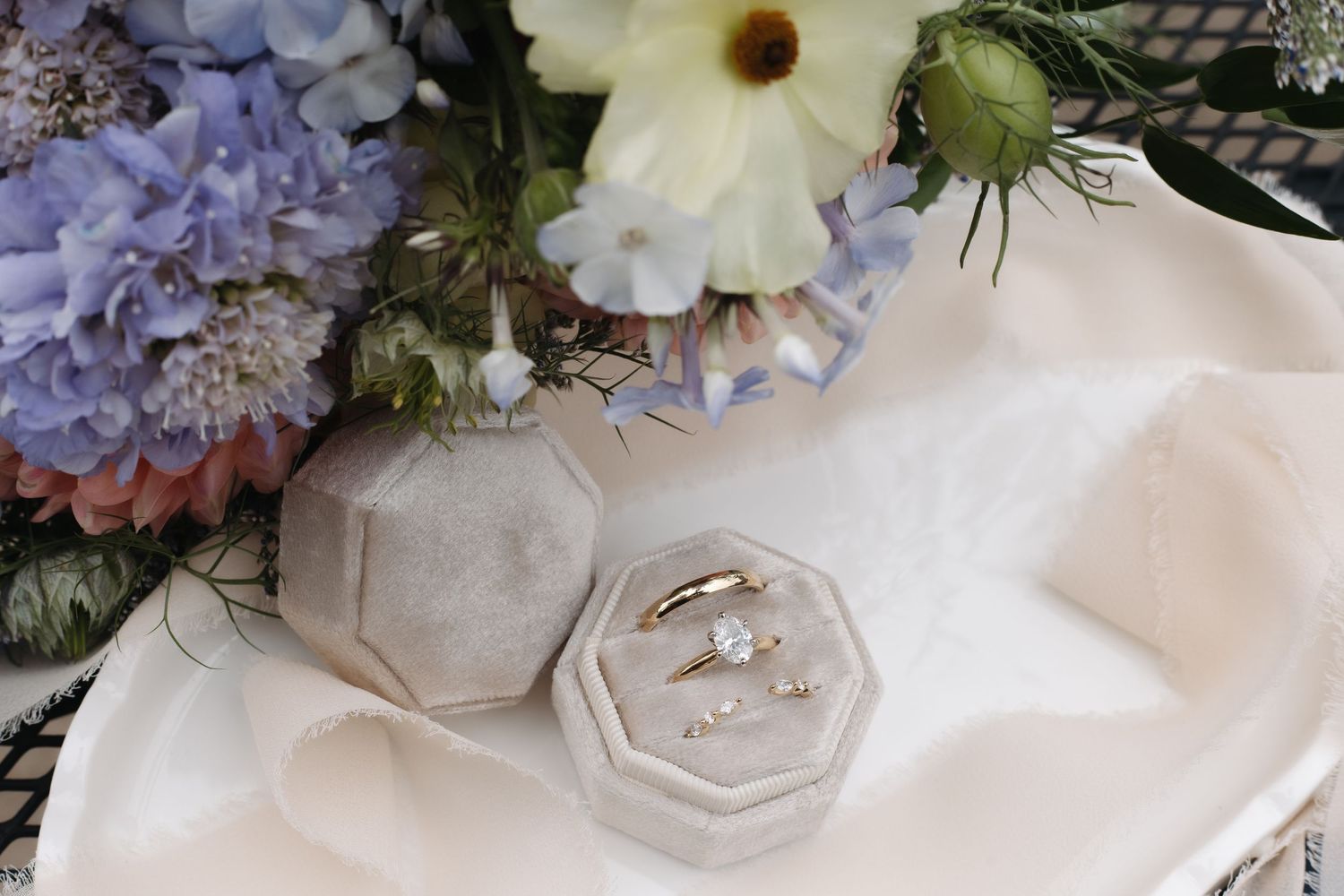 Wedding rings displayed in velvet box beside floral bouquet arrangement.