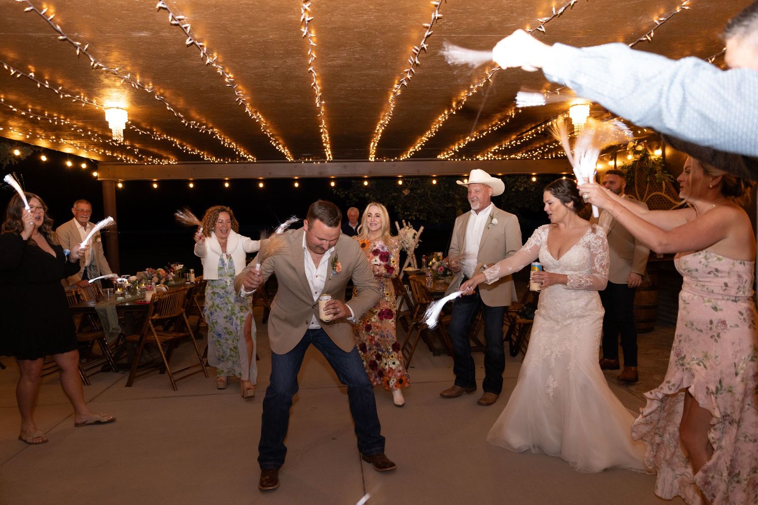 Joyful wedding reception sparkler exit under string lights in a rustic barn venue.