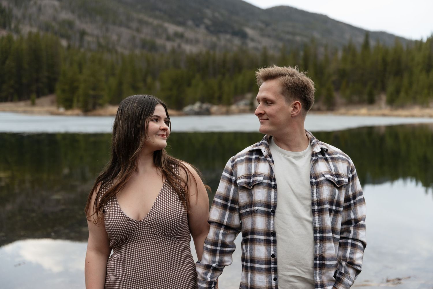 Happy couple sharing a romantic moment by a mountain lake surrounded by pine trees.