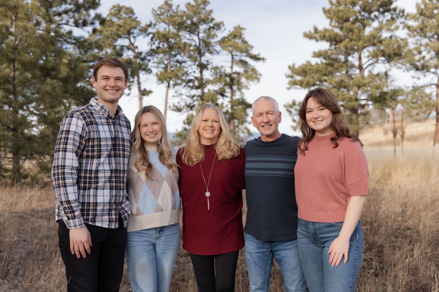 Family of five smiling together in a pine forest field during fall photo session.