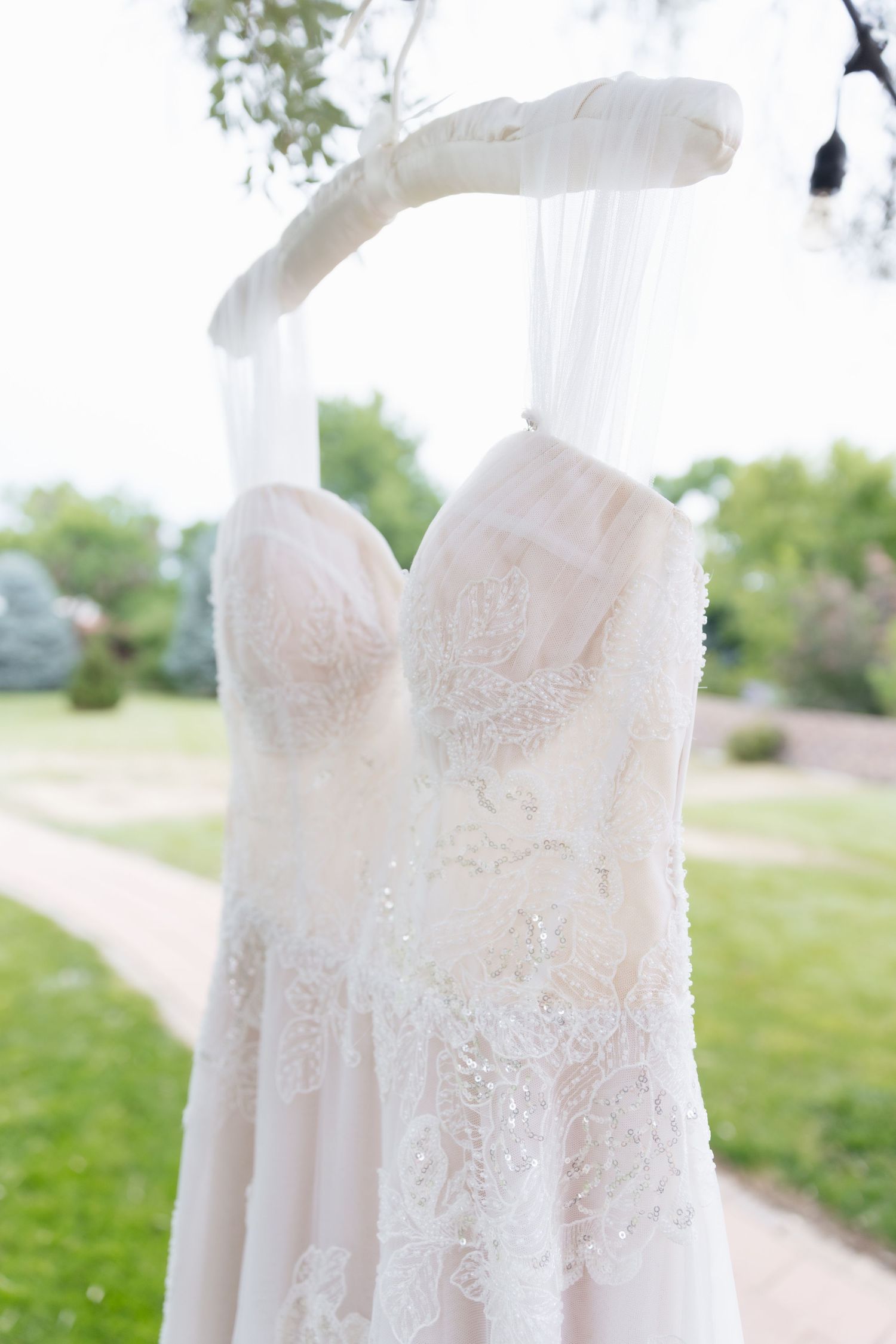 Elegant lace strapless wedding dress hanging outdoors on wooden hanger.