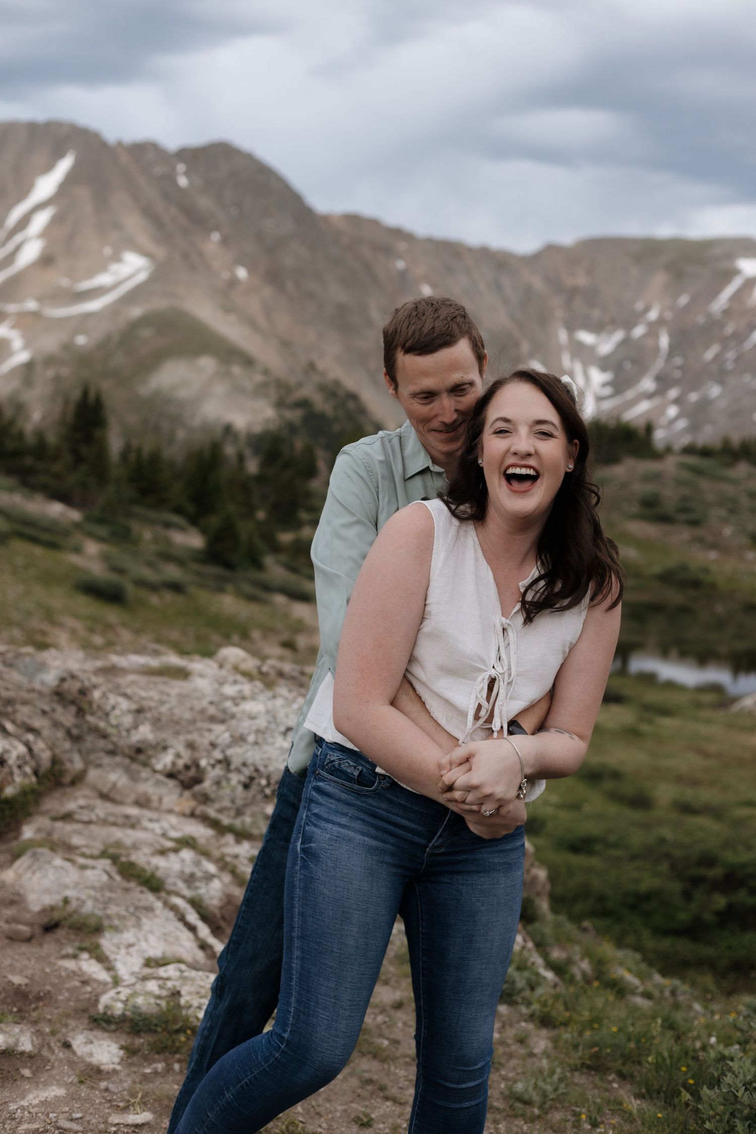 Joyful couple laughing and embracing in a high alpine meadow with snow-capped mountain peaks. Loveland Pass