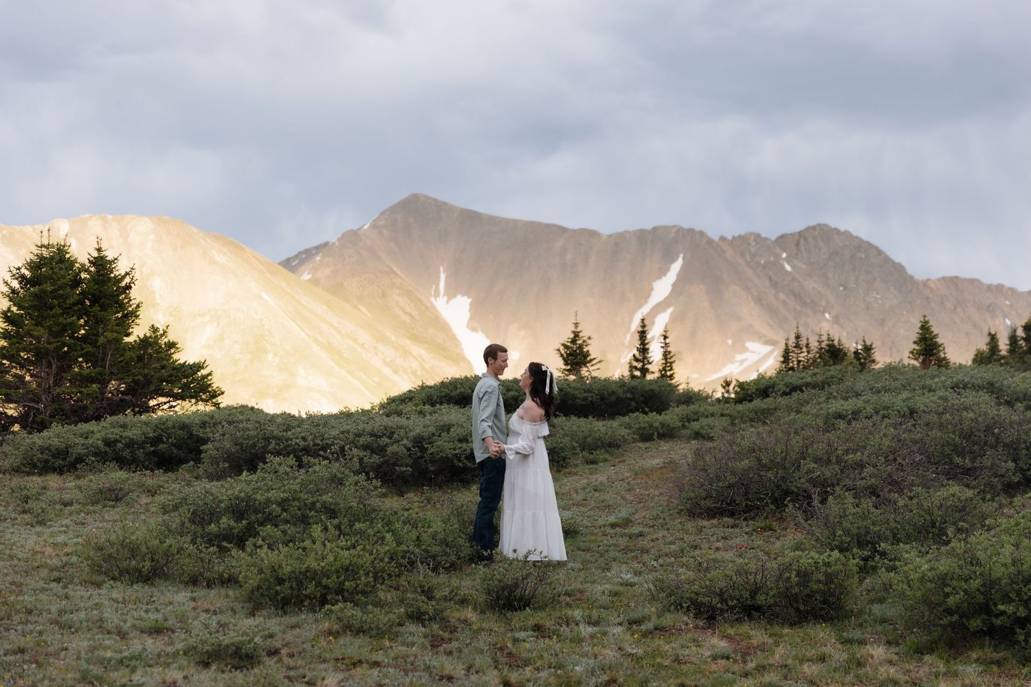 Bride and groom standing together in a lush alpine meadow with dramatic Colorado mountain backdrop. Loveland Pass