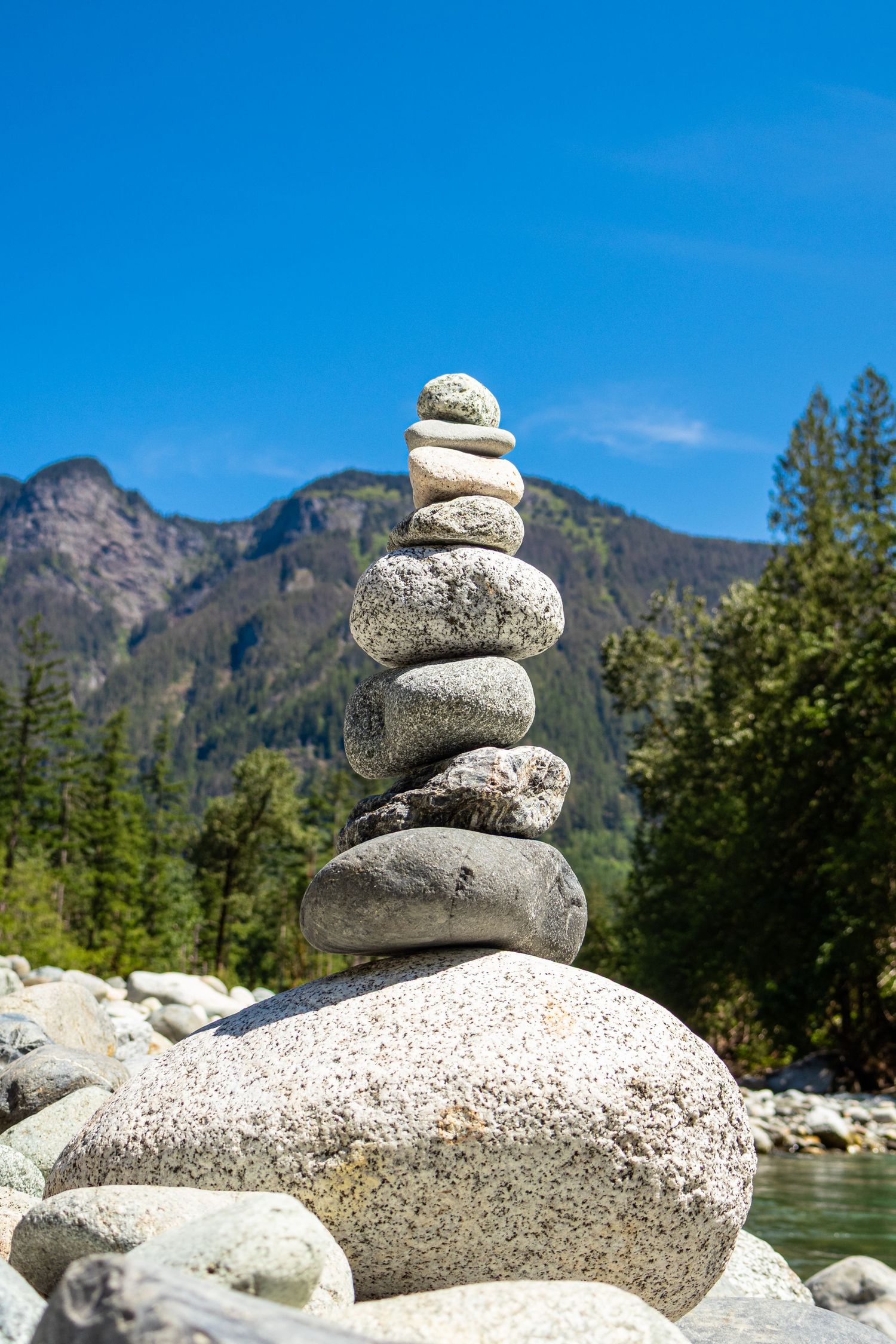 Balanced stack of smooth river rocks against a scenic mountain landscape with blue sky and green forest.