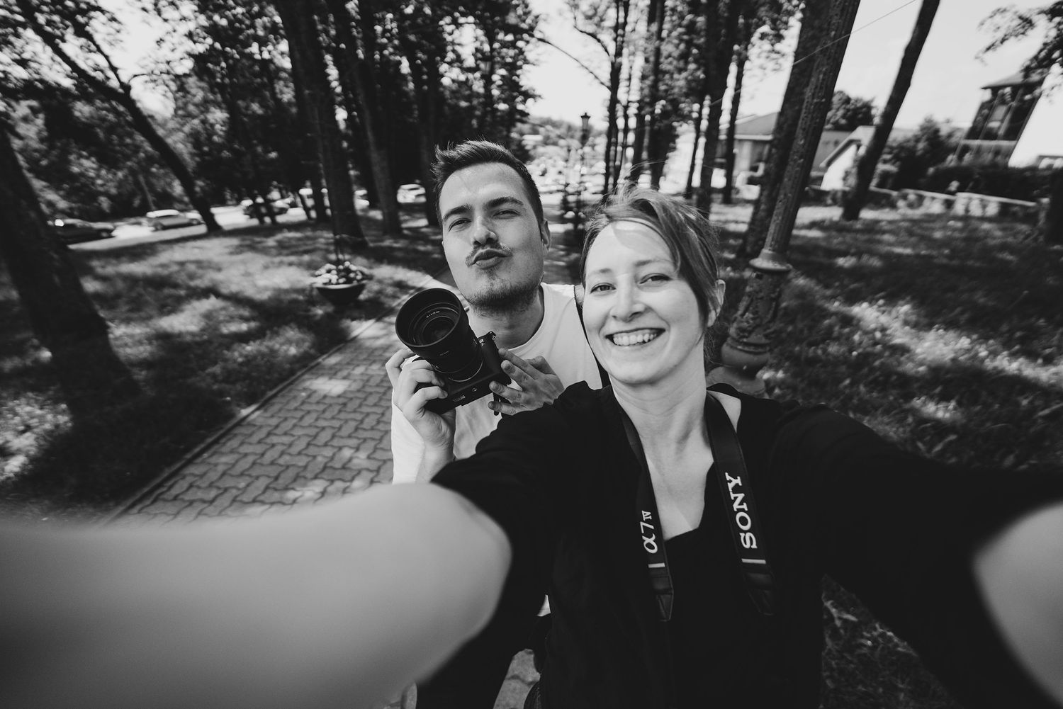 Couple laughing and embracing in a sunlit forest setting during a casual photo session.