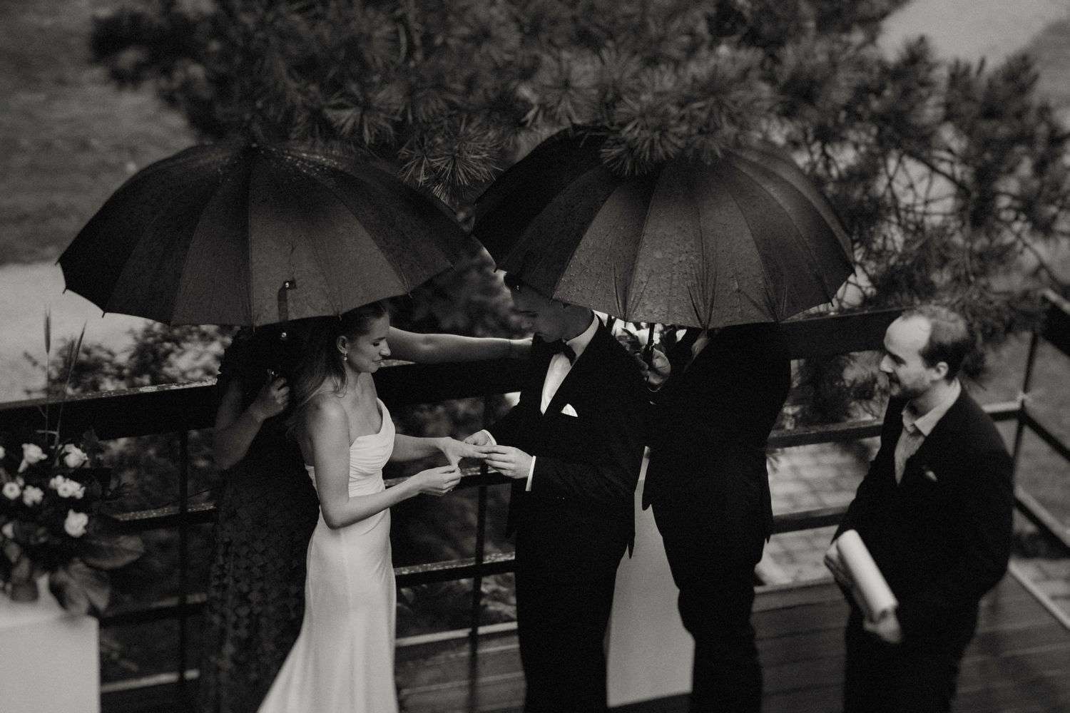 Wedding ceremony participants holding black umbrellas during an outdoor event.