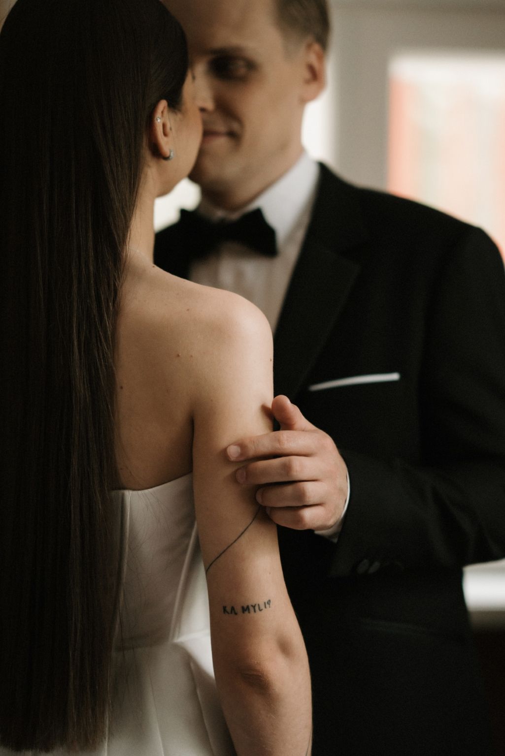Close-up of a couple embracing, showing a small arm tattoo and formal attire.