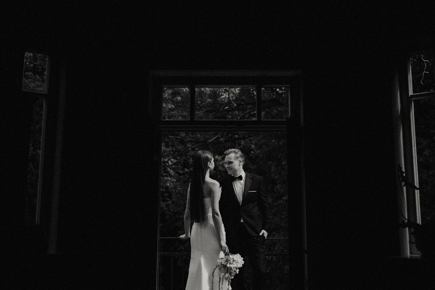 Artistic black and white wedding photograph captured through a dark window frame.
