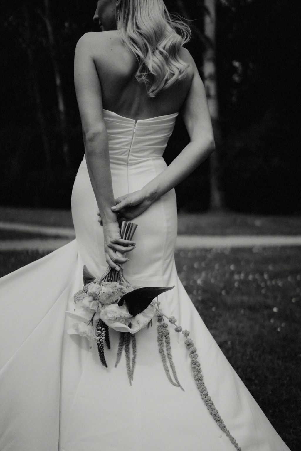Back view of a bride in white dress holding elegant bouquet with trailing ribbons.