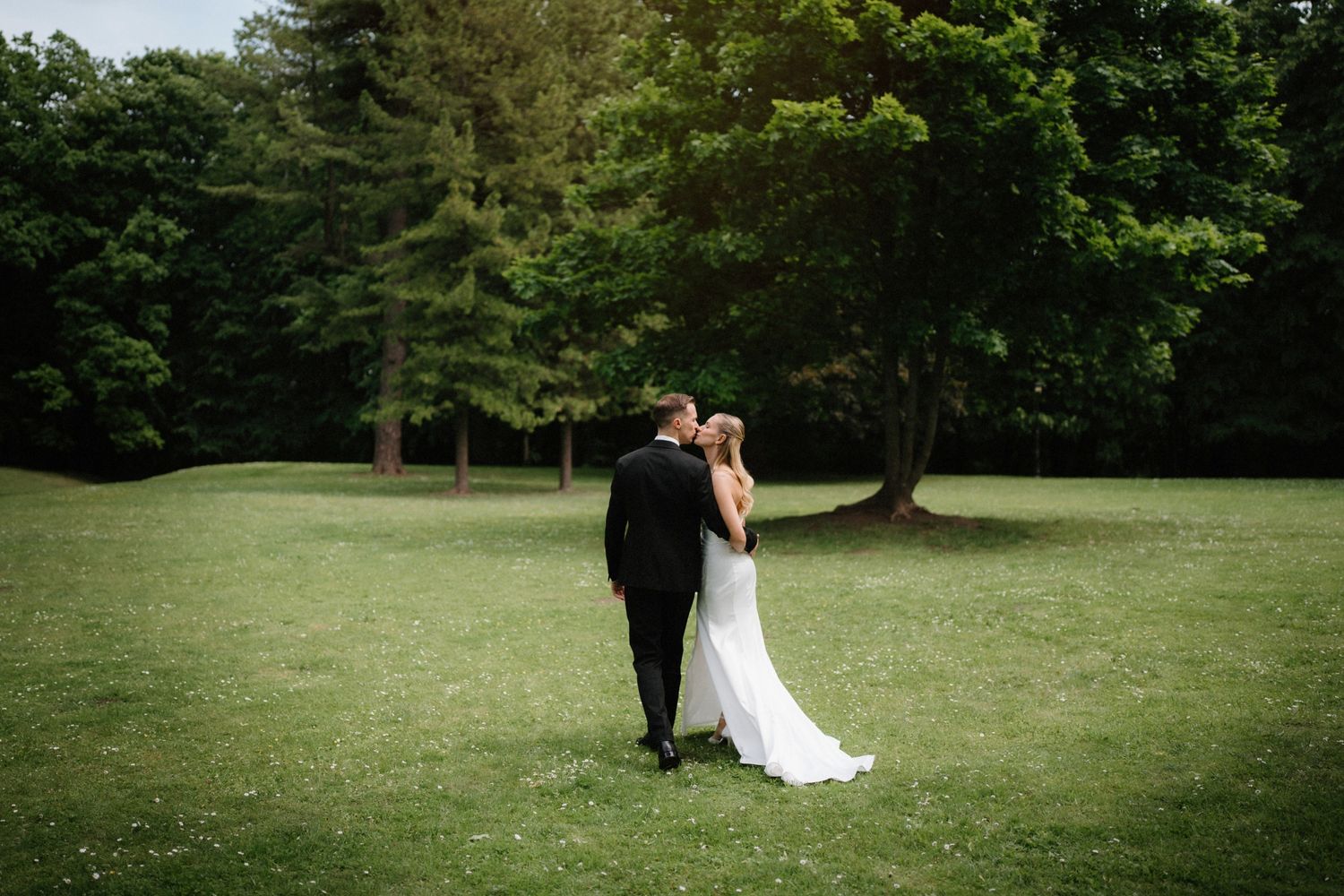 Newlyweds walking together on a lush green lawn surrounded by trees.