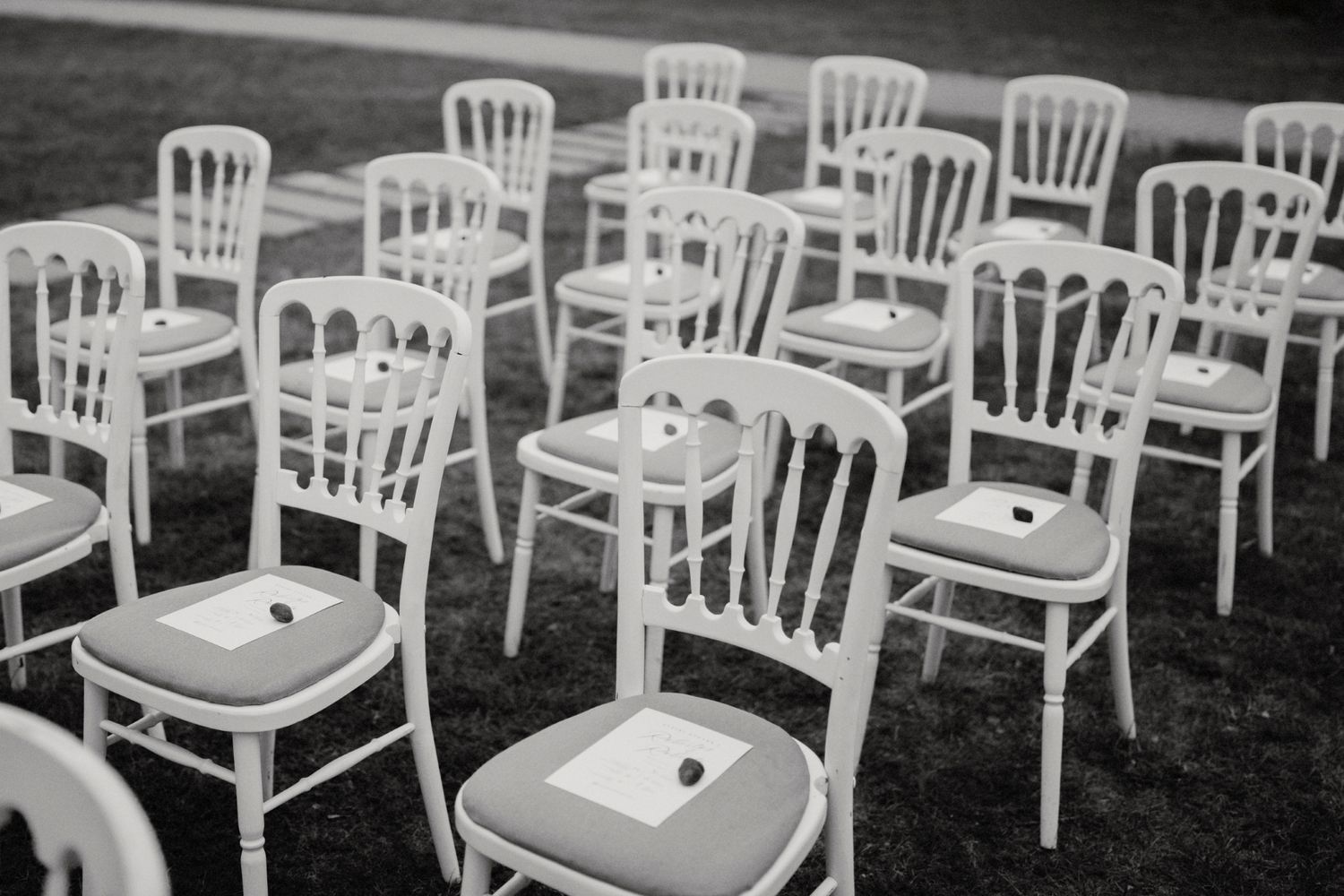 White wooden chairs arranged in neat rows on grass for an outdoor event.