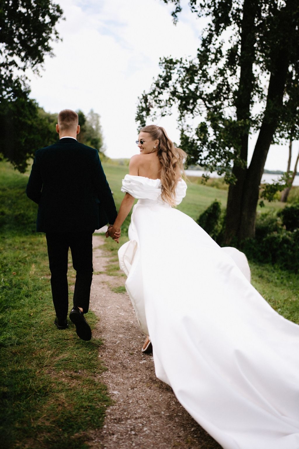 A couple walks along a nature path, with the bride's white dress flowing dramatically behind them.