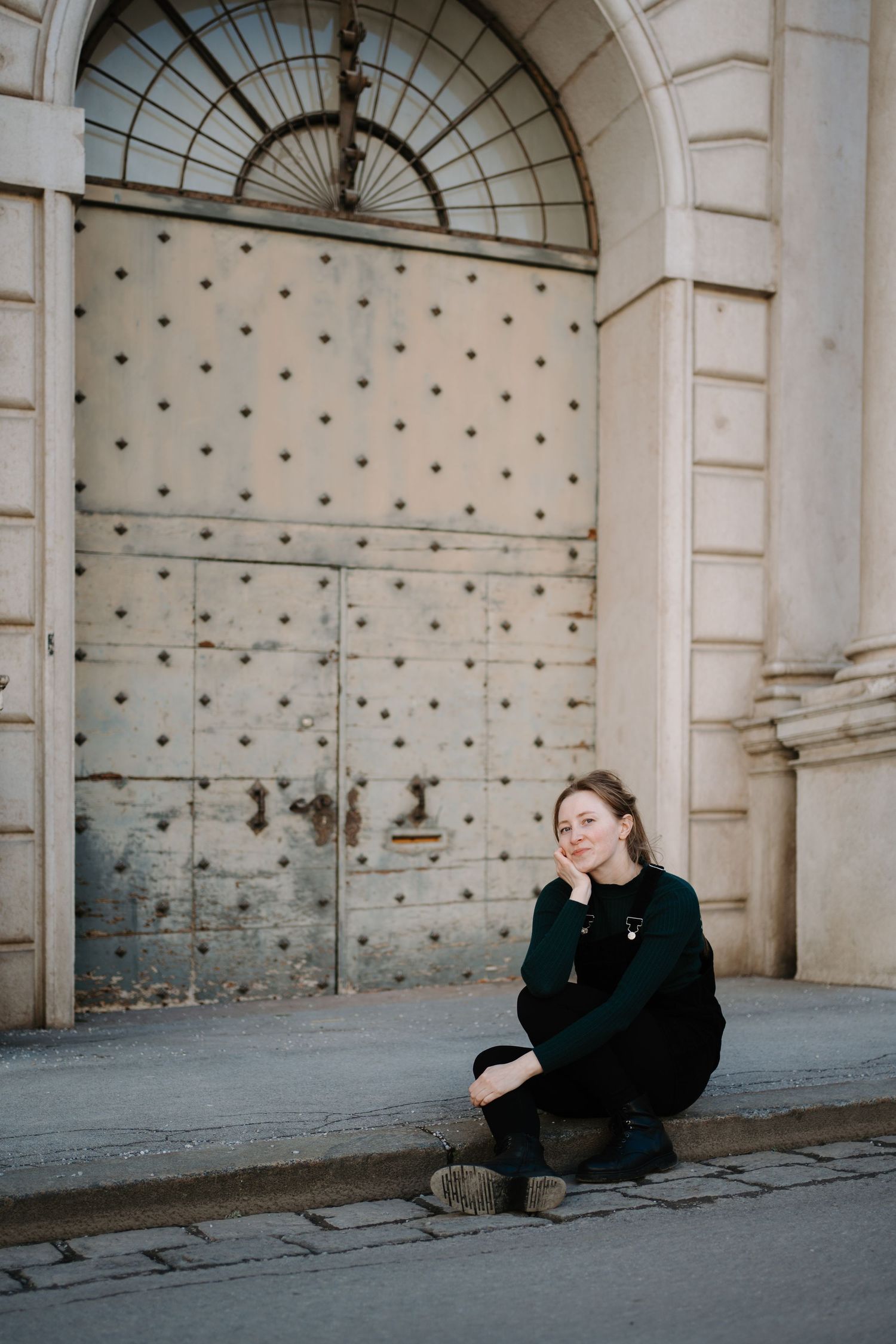 Person in black clothing sitting against an ornate architectural wall with arches and dotted pattern.