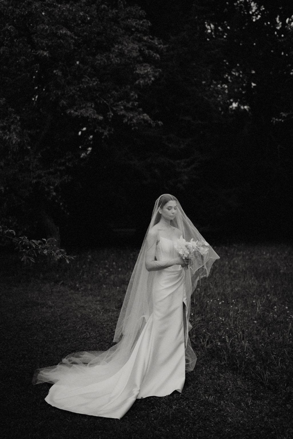 Elegant bride in a flowing white dress and veil poses in a garden setting.