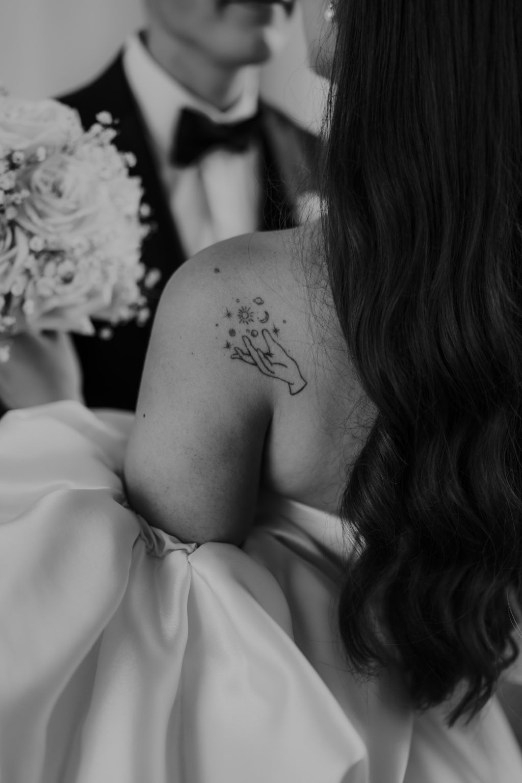Close-up details of an off-shoulder wedding dress and delicate tattoo artwork.