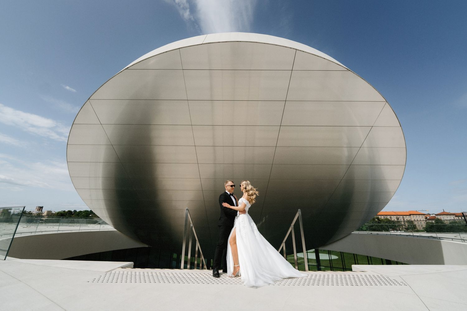 Modern curved architectural structure provides dramatic backdrop for outdoor wedding portraits.
