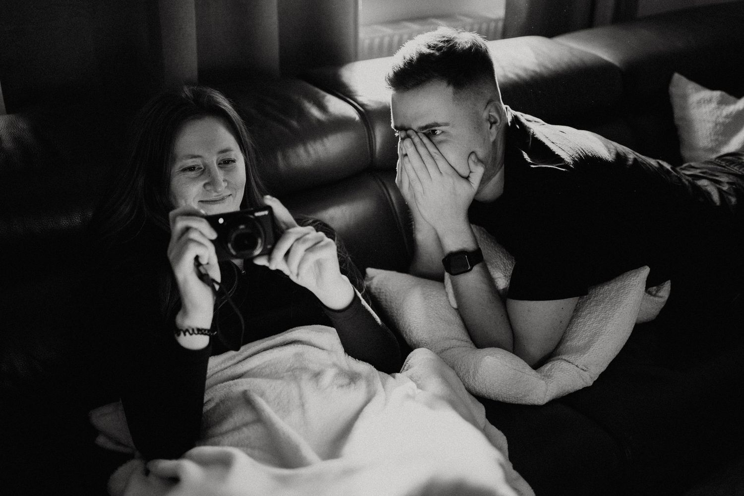 Black and white image of people relaxing on a couch in dim lighting.
