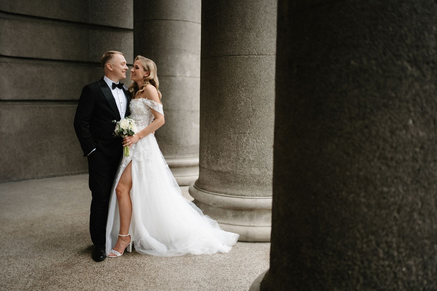 Wedding couple poses between classical stone columns in dramatic black and white photography.
