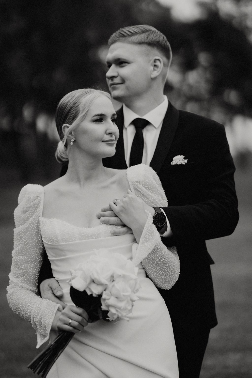 Elegant couple in formal wedding attire embracing outdoors in black and white.