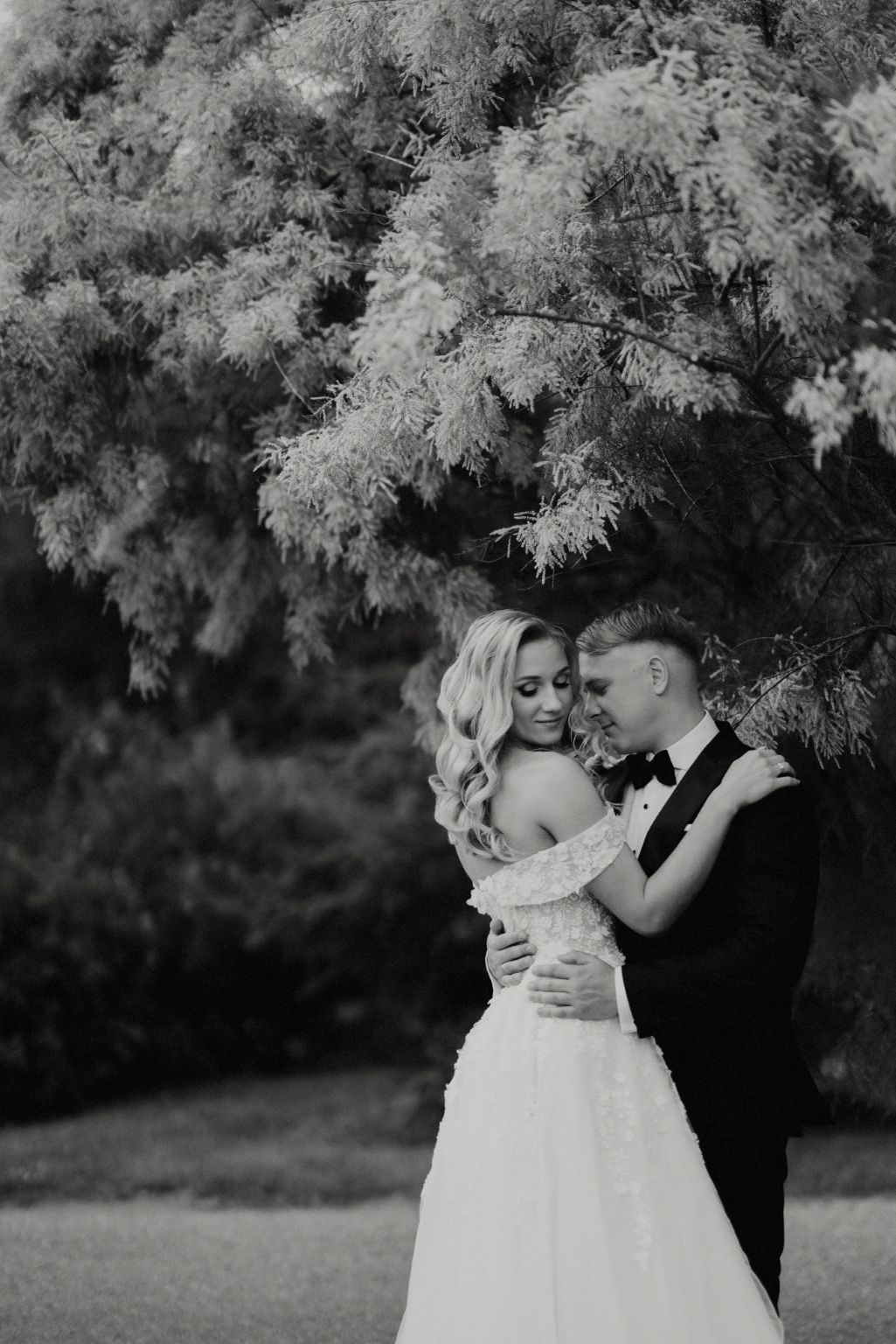 A romantic black and white wedding photo series showing an intimate embrace under trees.