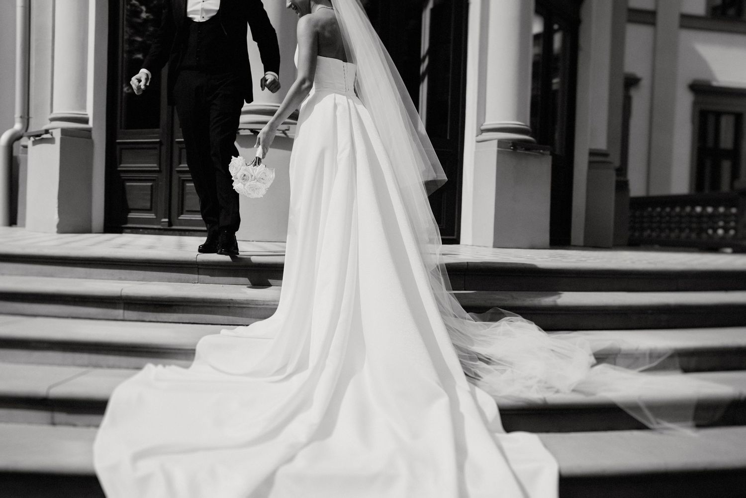 Elegant wedding dress train flowing across classic white architectural setting.