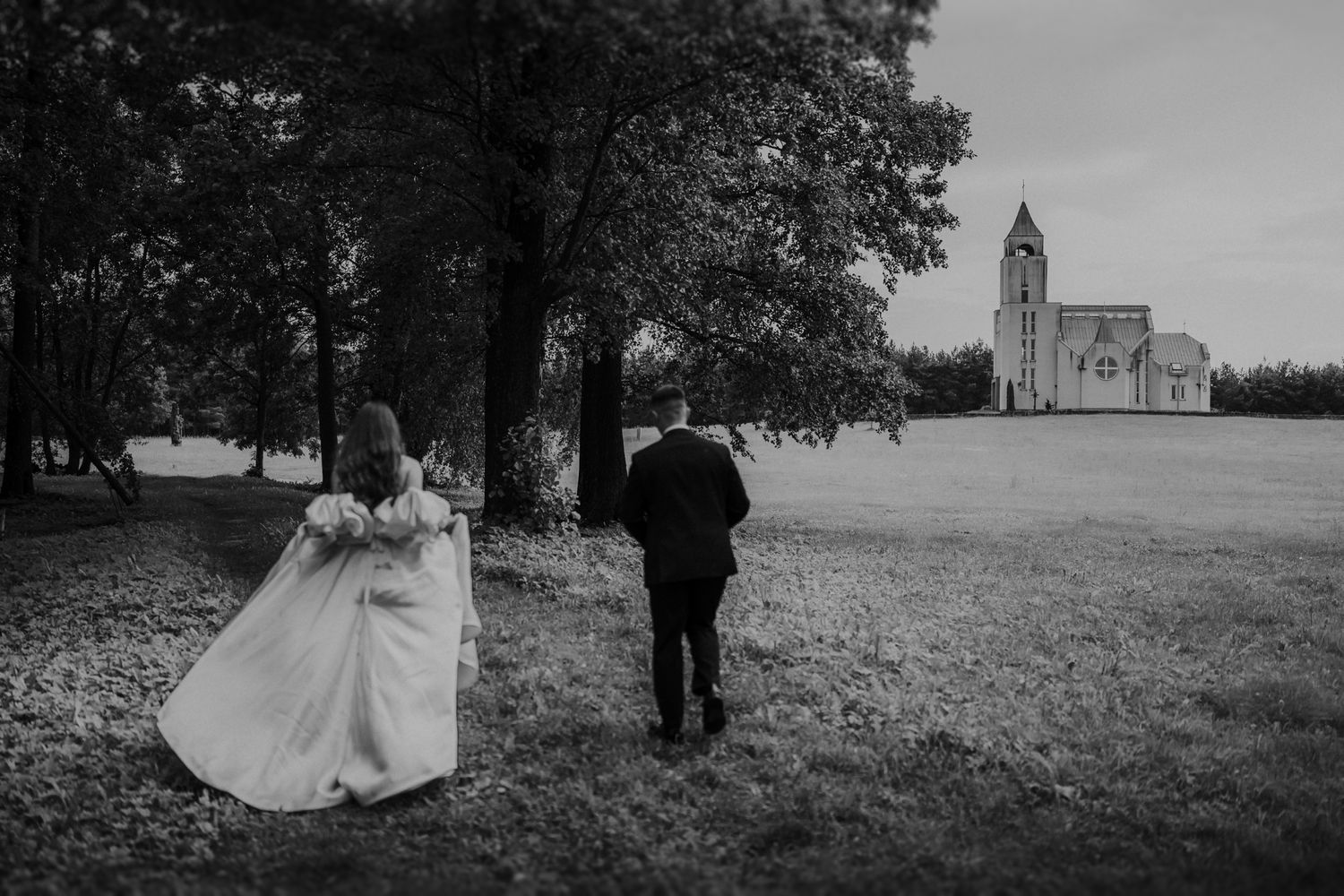 A black and white panoramic wedding scene with a church silhouette in the distance.