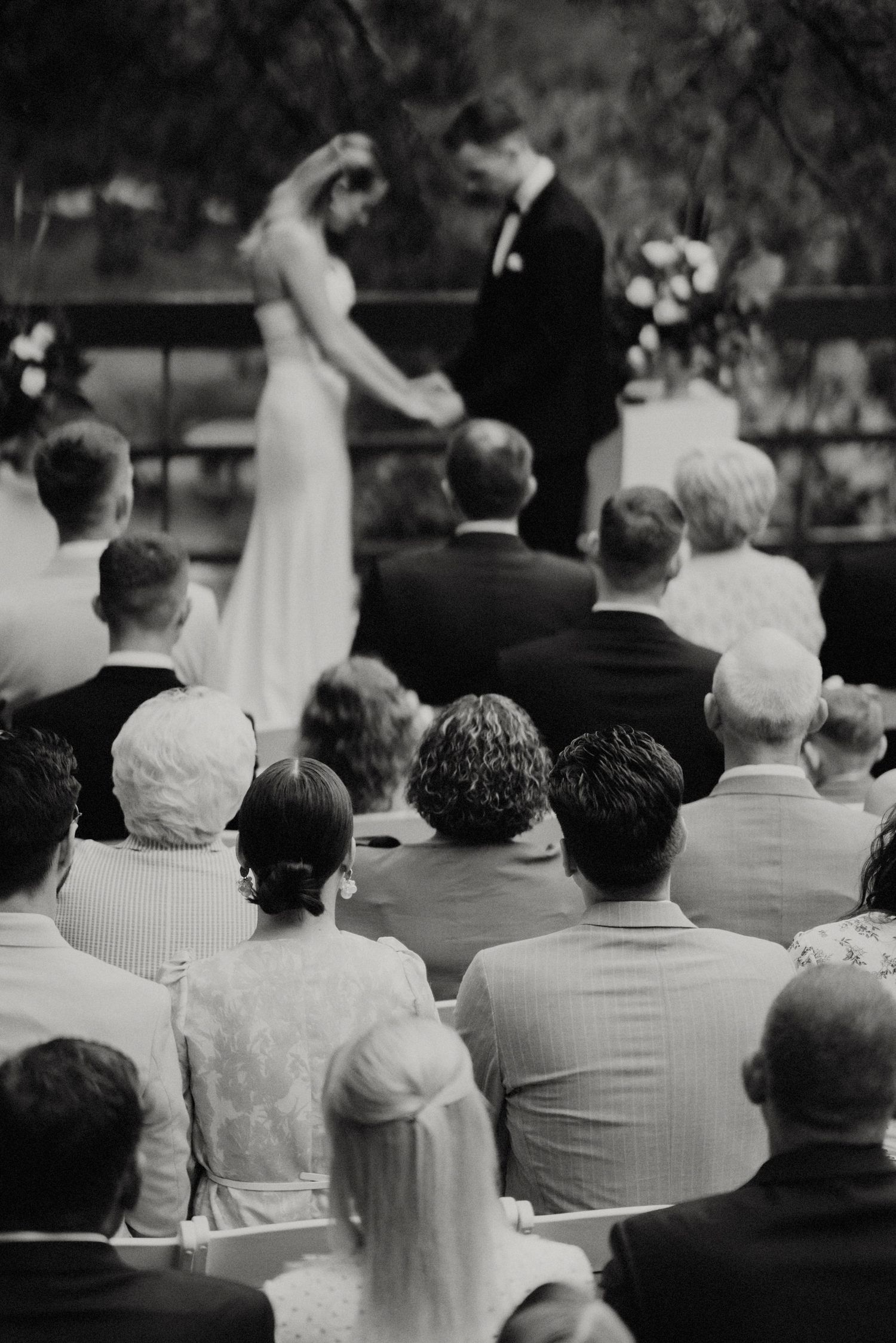 Black and white photo showing wedding ceremony guests seated in rows outdoors.