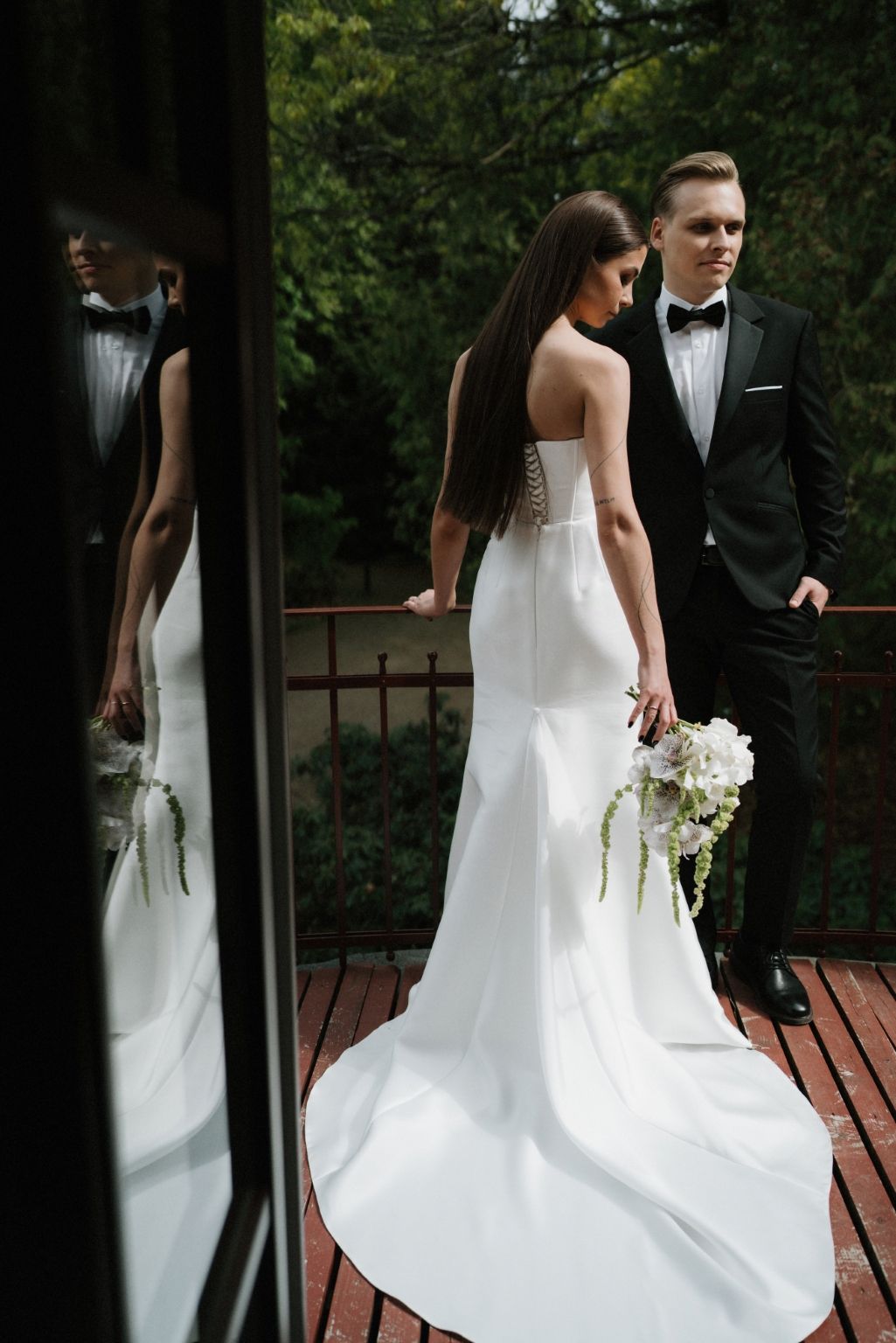 Elegant bride in minimalist white dress walks with groom on wooden deck.