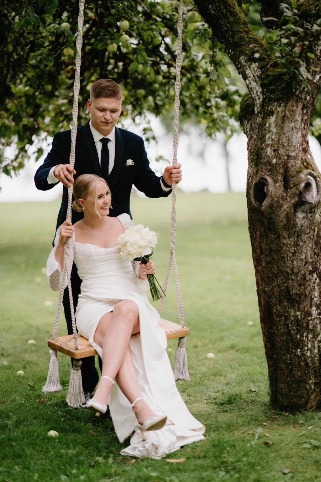 Couple enjoying a romantic moment on a decorated tree swing in a garden setting.