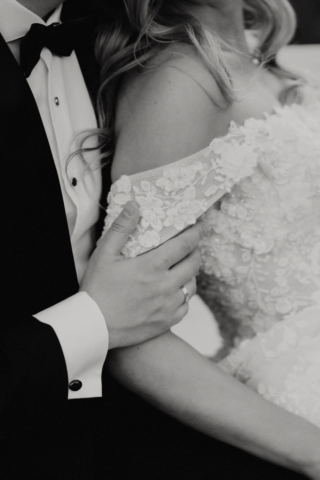 Intimate black and white close-up of wedding dress details and tender embrace.