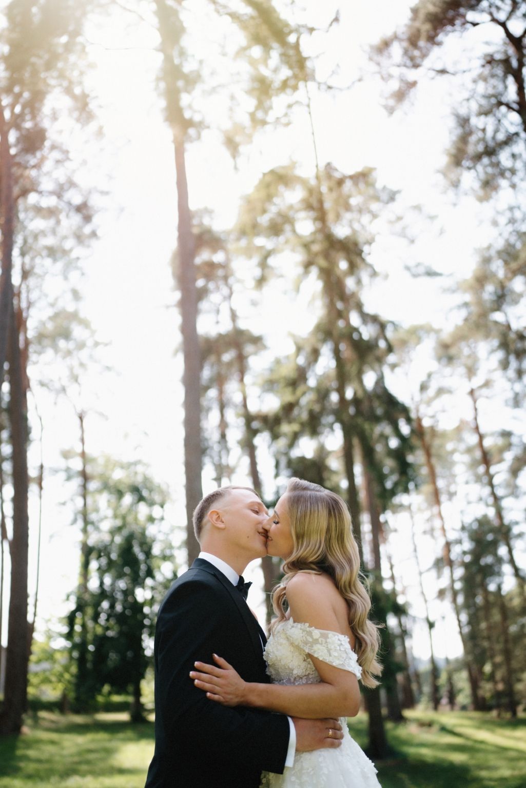 Sunlit wedding portrait in a forest with golden light filtering through the trees.